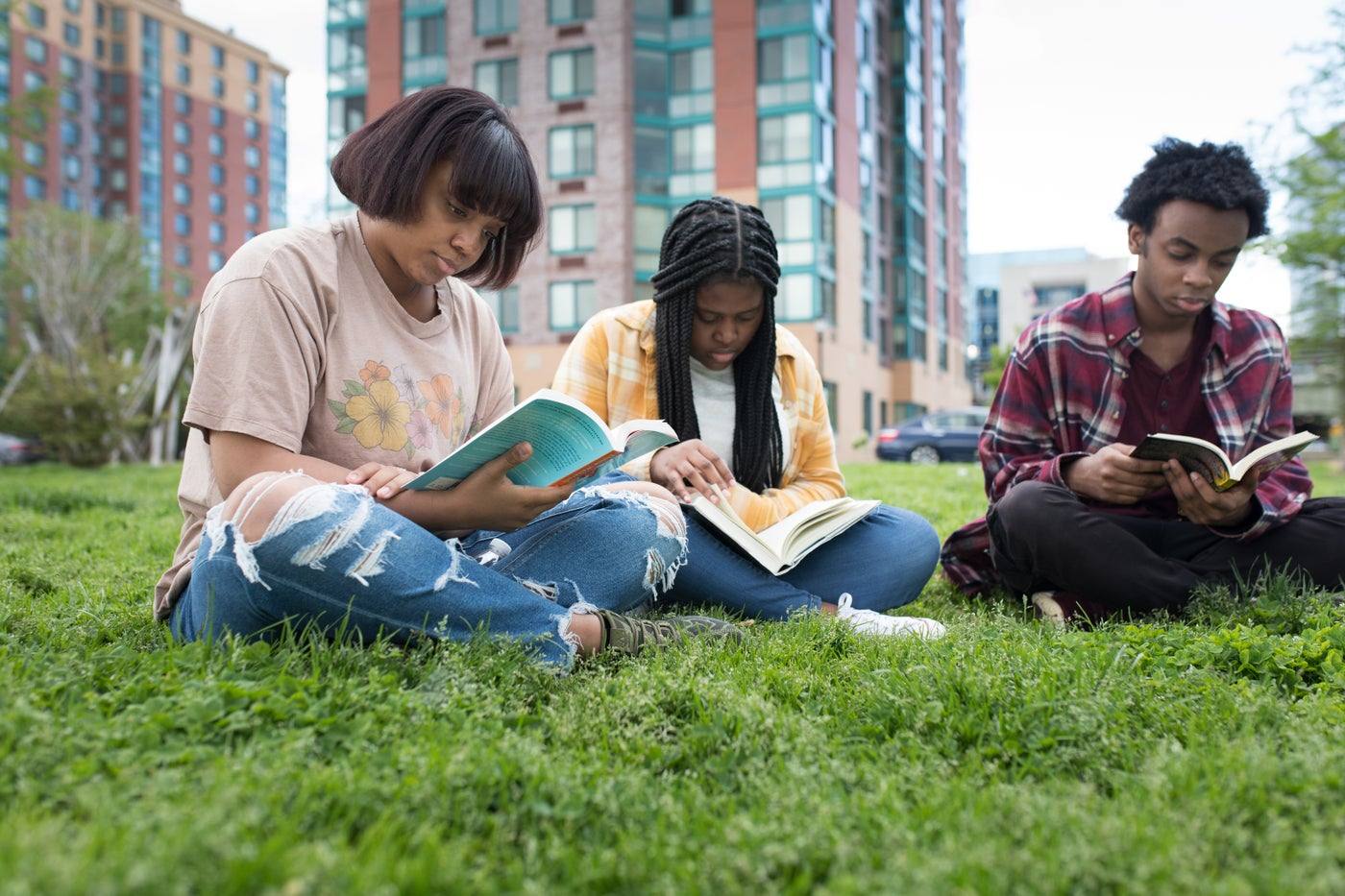 Young people reading together on the grass in a city park